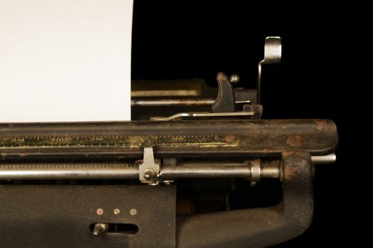 A closeup view of an antique typewriter machine from the mid 1900s with a blank piece of paper.