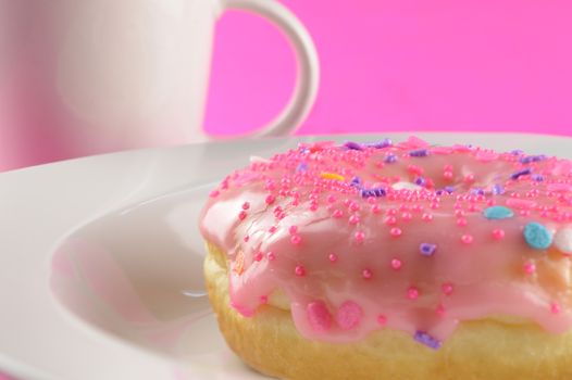 A low angle closeup of a freshly baked donut and coffee over a pink background.