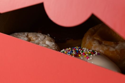 A closeup view of a slightly opened box of freshly baked donuts.