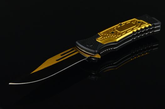 A black and gold pocket knife over a reflective surface.