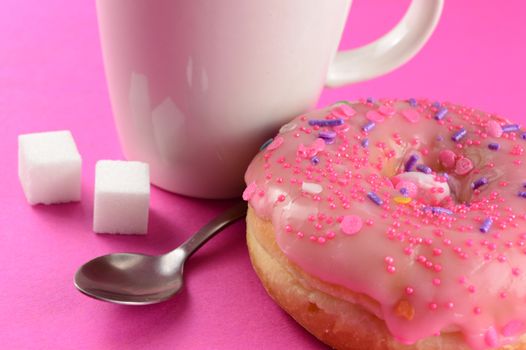 A closeup of a pink frosted donut and coffee for a quick break.