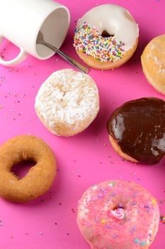 A bunch of donuts over a hot pink background with a coffee cup.