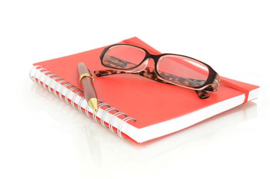 An isolated shot of a red notebook and pair of eye glasses over a white background.