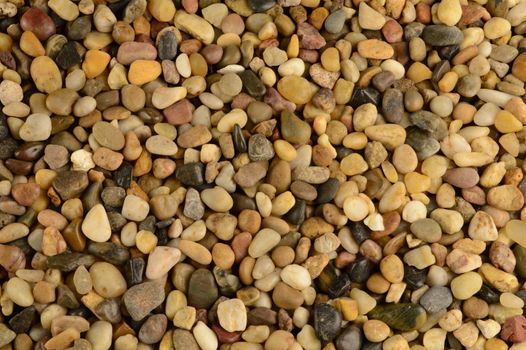 A closeup full frame view of some evenly lit washed clean river stones that are used as a landscaping material for footpaths and flowerbeds.