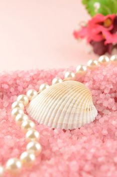 A sea shell and a string of pearls lay across a bed of pink bath salts for a warm inviting scene with a feminine touch.