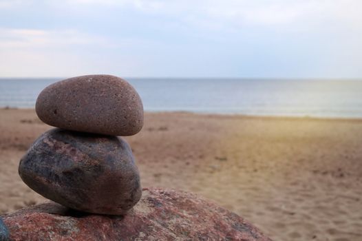 Two stacked natural rocks on top of a boulder on a sandy tropical beach in the distance