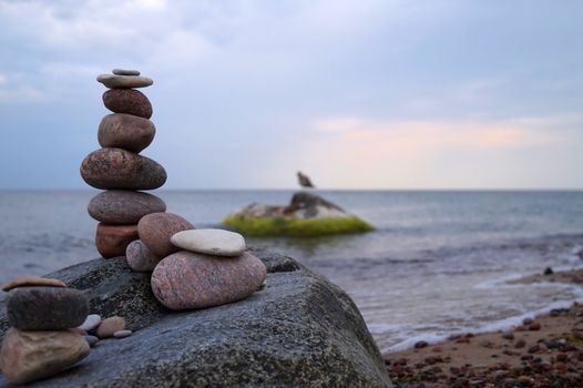 Tall balanced cairn of stacked of stones or rocks on a beach placed on top of a boulder overlooking the ocean and gentle waves at sunset