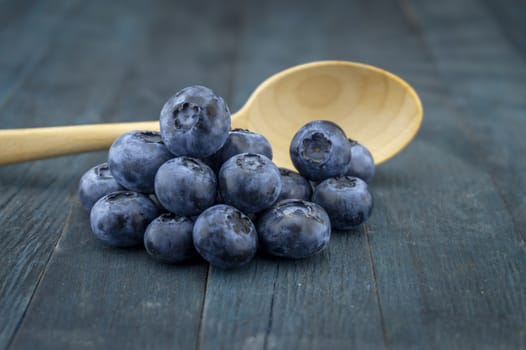 Bunch of fresh blueberries and wooden spoon on blue rustic board, low angle selective focus and free copy space for text