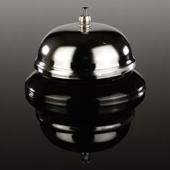 A standard desktop call bell over a gradient reflective surface.