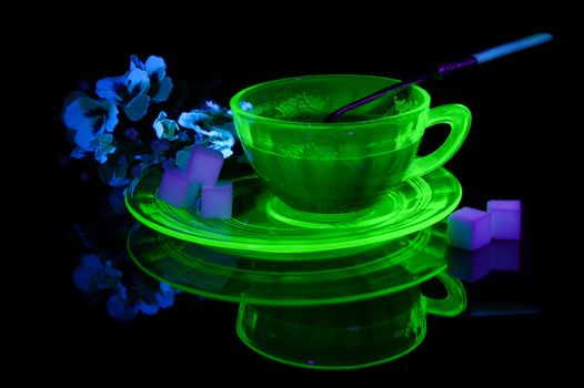 A glowing Uranium Glass Teacup and Saucer under some ultraviolet light to show its unique properties.