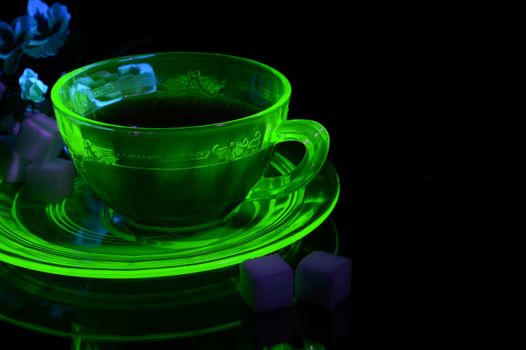 A glowing Uranium Glass Teacup and Saucer under some ultraviolet light to show its unique properties.