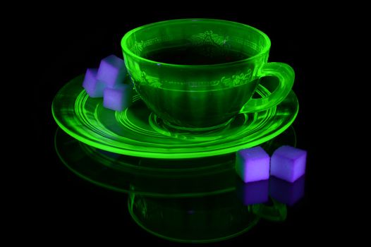 A glowing Uranium Glass Teacup and Saucer under some ultraviolet light to show its unique properties.