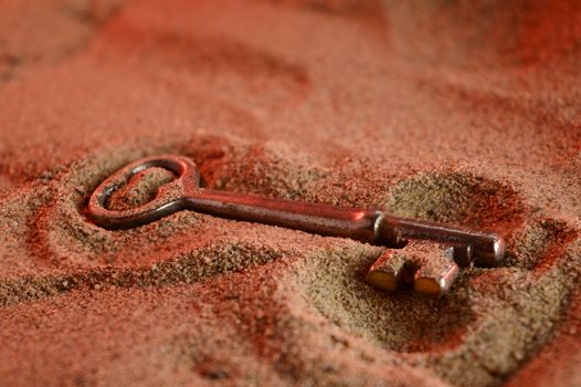 An ancient skeleton key is revealed at the surface of a sandy terrain.