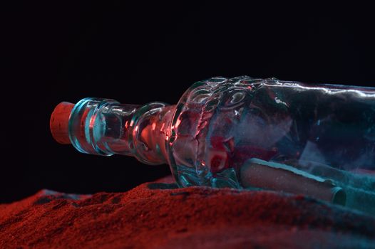 A closeup low angle shot of a message in a bottle revealed in the sandy shoreline during the night time light.