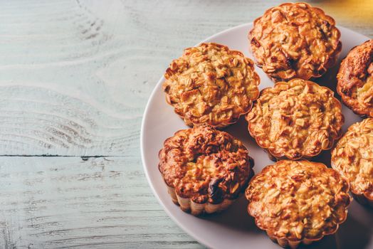 Cooked oatmeal muffins on white plate over light wooden background.