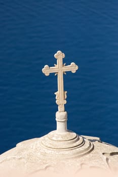 A roof of a church with a cross high up over the mediterranean sea, seen on Santorini island