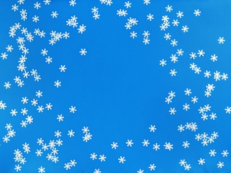 Scattered white snowflakes on blue background. Simple flat lay with copy space. Stock photo.