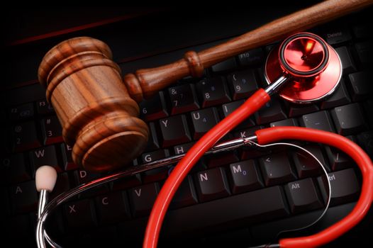 An overhead view of a legal wood gavel and Doctors stethoscope resting on top of a black keypad and some red gel lighting striking the scene.