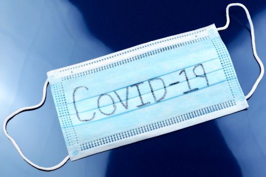 A face mask with the handwritten word Covid-19 for the global Coronavirus outbreak starting in 2019.