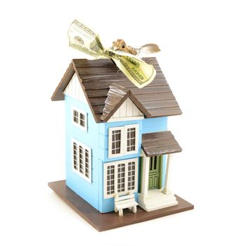 A conceptual image with a small bird holding a hundred dollar bill in its beak while resting on top of a miniature house.