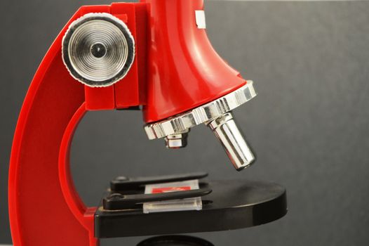 A closeup on a red microscope over a black gradient background.