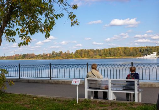 Two elderly women sit on a bench by the river in a city Park. Relaxation. The concept of loneliness.