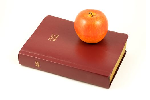 An isolated Holy Bible and red apple over a white background.