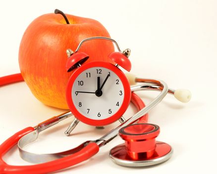 An apple and alarm clock and stethoscope come together for representing a clinical checkup time.