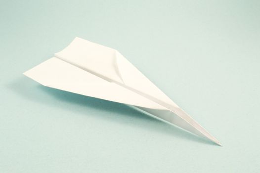 A folded white paper plane flying over a blue background.