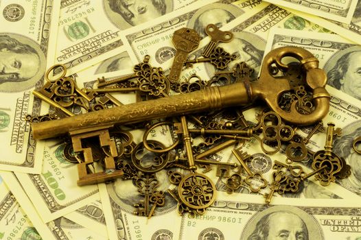A pile of brass keys with a larger dominant one centered on a background of American hundred dollar bills for creating a wealth strategy concept.