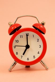 An isolated over pink background image of a red alarm clock set to seven oclock.