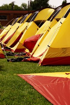A place has setup several tents in order to air dry them after a camping trip has rendered them all wet due to rainy weather conditions during the time of the trip.