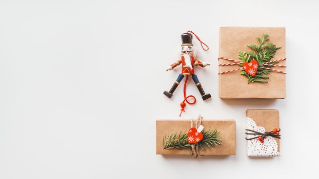 Christmas DIY presents wrapped in craft paper and wooden Nutcracker toy. Decorations on New Year gifts. Festive background. Winter holiday spirit. White background with copy space.