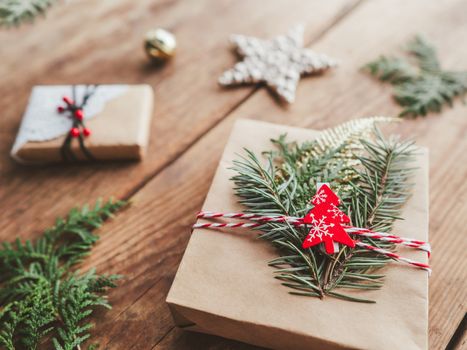 Christmas DIY presents wrapped in craft paper with fir tree twigs. Red decorations in shape of Christmas tree, stars. New Year gifts on wooden background. Winter holiday spirit.