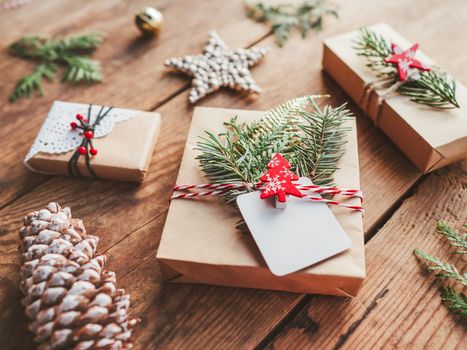 Christmas DIY presents wrapped in craft paper with fir tree twigs. Red decorations in shape of Christmas tree, stars. New Year gifts on wooden background. Winter holiday spirit.