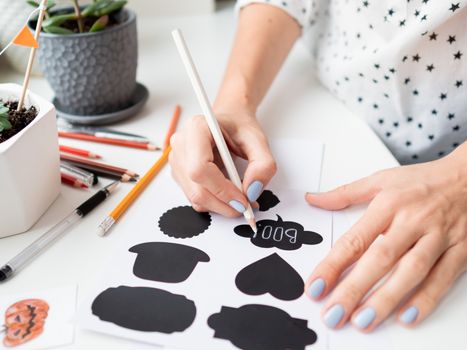 Woman writes Boo! on decorative black stickers for flower pots. Handmade decorations for Halloween.