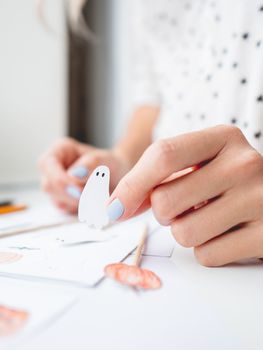 Woman draws pumpkins and ghosts. Handmade decorations for Halloween 2020. DIY stickers on for flower pots. Socially-Distanced Halloween at home.