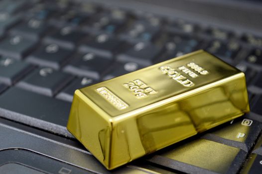 Closeup of a 200 gram bar of pure gold sitting on a laptop to illustrate the ease of online trading and purchase of the precious metal.