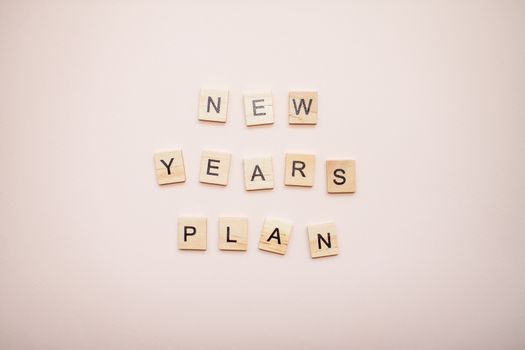 The inscription new years plan from wooden blocks on a light pink background.