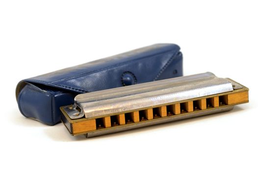 An isolated over a white background still-life image of a harmonica musical instrument and its original blue case.
