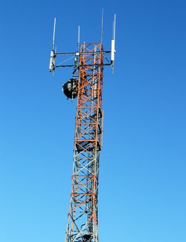 A glance upwards at an antenna located ontop of a blue sky background.