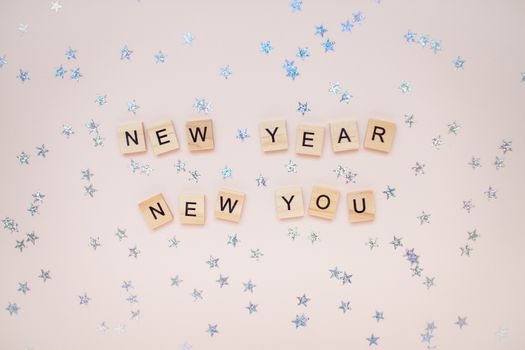 The inscription new year new you from wooden blocks on a light pink background. Silvery stars on a light pink background.