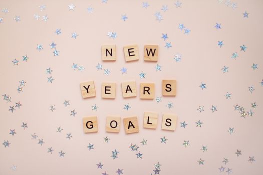 The inscription new years goals from wooden blocks on a light pink background. Silvery stars on a light pink background.