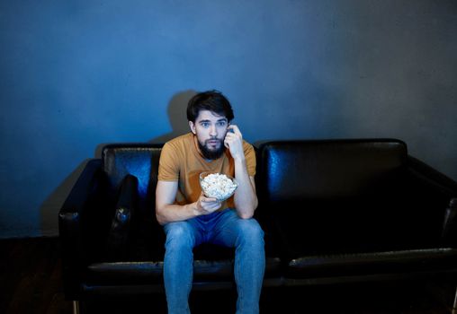 A man sits on a sofa indoors and watches TV front view. High quality photo