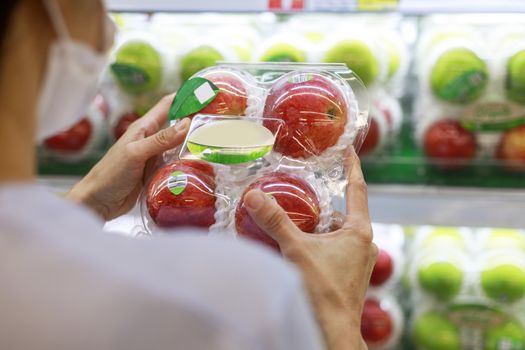 Women long hair wear protective face mask hands holding green apples ipackage. Asian female shopping at supermarket, Grocery to buy some food. New normal after covid-19 concept.