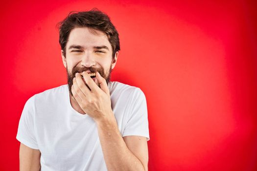 A man in a white T-shirt with a beard gestures with his hands emotions red background. High quality photo