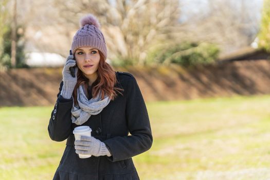 A gorgeous blonde model enjoys a winters day outdoors while drinking her favorite drink and talking on her cellphone