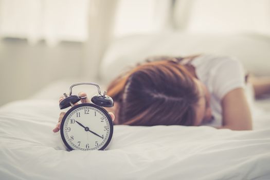 Beautiful asian young woman turn off alarm clock in good morning, wake up for sleep with closeup foreground alarm clock, relax and lifestyle concept.