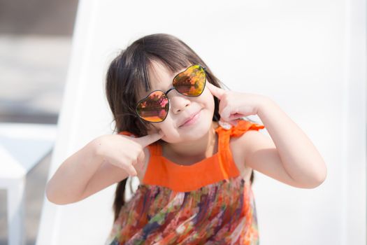Beautiful portrait little girl asian of a smiling sitting at swimming pool, kid leisure and joyful wear glasses in outdoor.