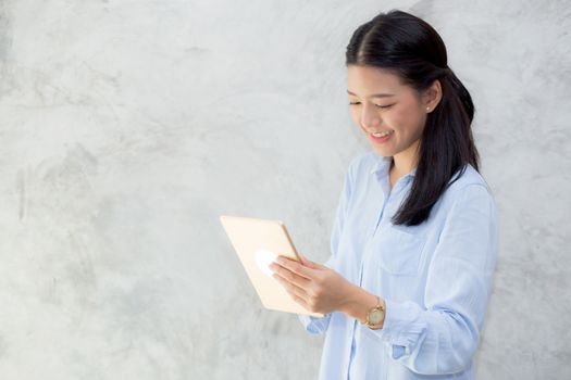 Beautiful young asian woman touch tablet computer and smile standing on cement background, freelancer girl with social media online, communication concept.